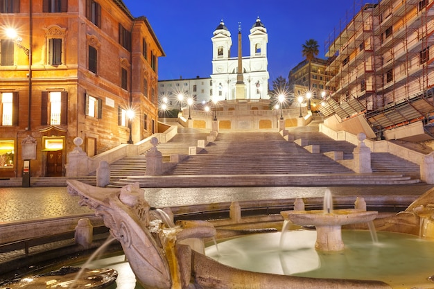 Escalera monumental de la Plaza de España, visto desde la Piazza di Spagna, y la fuente barroca temprana llamada Fontana della Barcaccia o Fuente del barco feo durante la hora azul de la mañana, Roma, Italia.