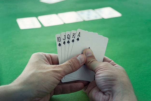 Foto la escalera real es la mejor combinación ganadora en el póquer. ganar en el casino. suerte en el juego. jugando a las cartas en la mano de un hombre en el fondo de una mesa de juego de casino.