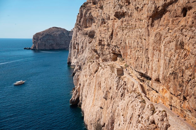 Escalera en roca caliza a la cueva de Neptuno de estalactitas Barco saliendo de Grotte di Nettuno en Cerdeña