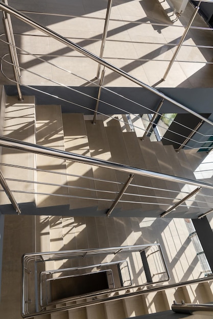 Escaleras en un edificio de oficinas de hormigón en tonos neutros cubiertas de baldosas de cerámica con barandillas de metal brillante