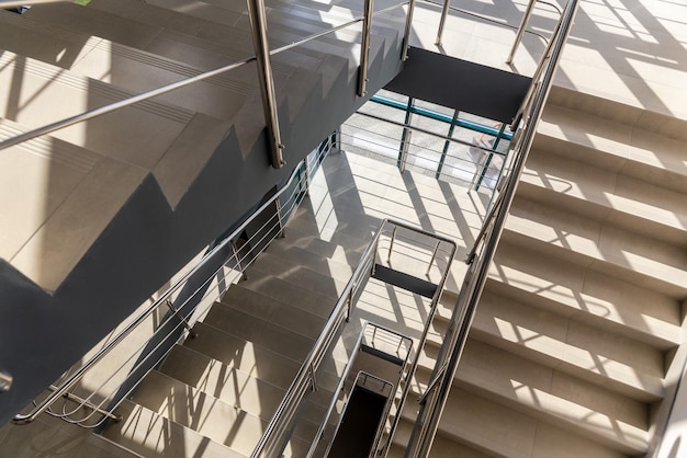 Escaleras en un edificio de oficinas de hormigón en tonos neutros cubiertas de baldosas de cerámica con barandillas de metal brillante