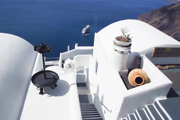 Escaleras en el edificio con vistas al mar mediterráneo con barco desde el techo de la casa o iglesia en Santorini, Grecia