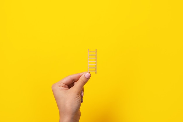 Foto escaleras de madera en mano sobre fondo amarillo, concepto de crecimiento profesional