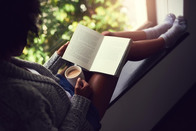 Escapando en la narración Toma de una joven no identificable leyendo un libro mientras disfruta de una taza de café en casa