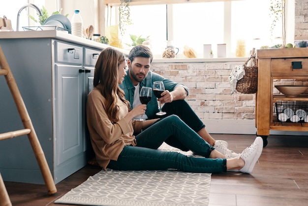 Foto escapando de todo. hermosa joven pareja bebiendo vino mientras está sentado en el piso de la cocina en casa