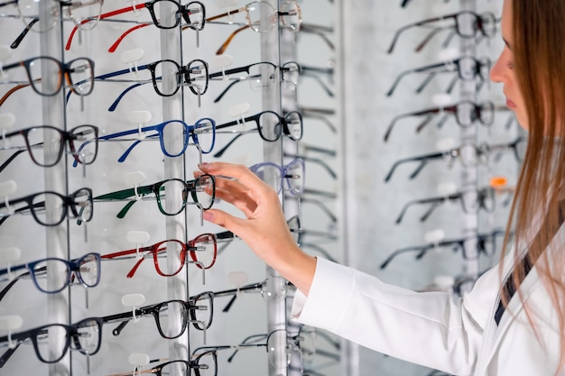 Escaparate con anteojos en tienda oftálmica moderna. Manos de mujer con gafas. De cerca.