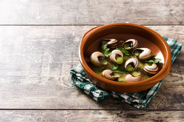 Escargots de Bourgogne in brauner Schüssel auf Holztisch, Kopienraum