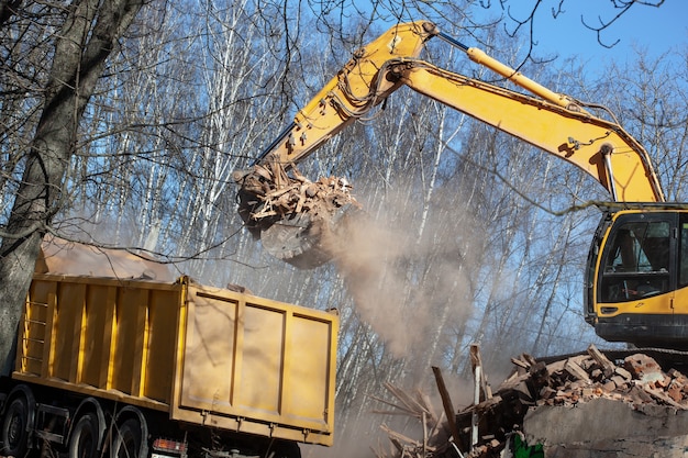 Foto escavadeira amarela carregando um caminhão basculante com entulho e lixo após a demolição do edifício