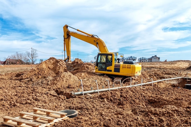 Escavadeira cava trincheiras em um canteiro de obras Trincheira para colocação de canos de esgoto externos Sistema de drenagem de esgoto para um edifício de vários andares Cavando a fundação do poço