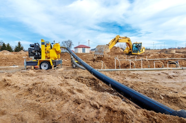 Escavadeira cava trincheiras em um canteiro de obras Trincheira para colocação de canos de esgoto externos Sistema de drenagem de esgoto para um prédio de vários andares Cavando a fundação do poço