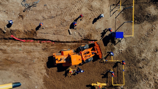 Escavadeira de vista aérea e trabalhadores da construção civil trabalhando no canteiro de obras em campo aberto colocação de tubos em trincheiras para gaseificação ponto superior do disparo reparo e restauração do suprimento de gás natural