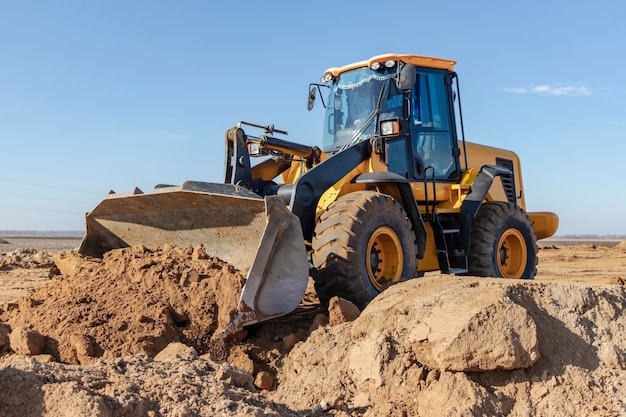 Escavadeira ou carregador move a terra no canteiro de obras contra o céu azul Uma máquina de terraplenagem está nivelando o local Equipamento pesado de construção para terraplanagem