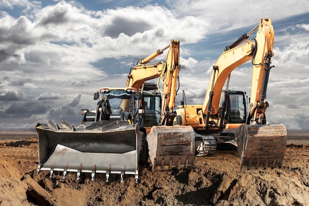 Escavadeira ou carregador move a terra no canteiro de obras contra o céu azul Uma máquina de terraplenagem está nivelando o local Equipamento pesado de construção para terraplanagem