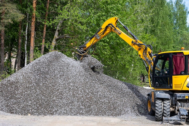Escavadeira pega um balde de pedra britada de uma grande pilha de escombros