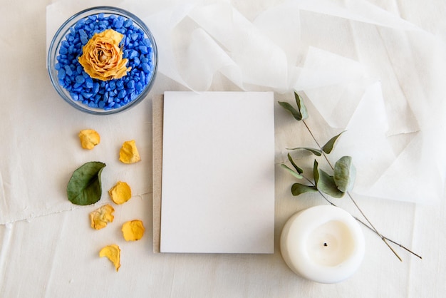 Escena de boda de verano de un diseño de papelería Una tarjeta de felicitación vertical vacía un sobre de papel artesanal y ramas de olivo aisladas sobre un fondo de mesa blanca Vista superior del apartamento mediterráneo femenino