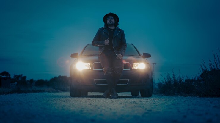 Escena cinematográfica de un coche con un hombre con sombrero y chaqueta.