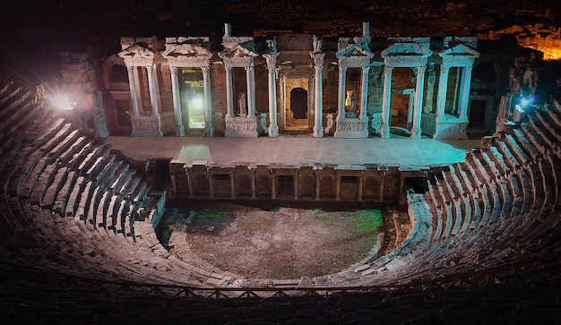 Escena y columnas con esculturas del antiguo anfiteatro en Hieropolis por la noche