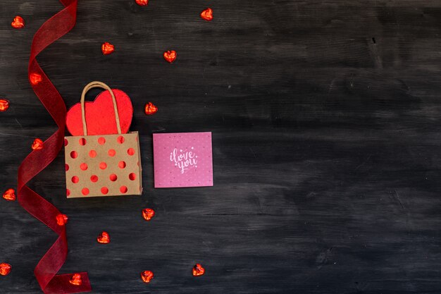 Escena del día de San Valentín con caja de regalo, corazones diferentes, tarjeta de felicitación y cinta roja sobre un fondo oscuro de la madera.