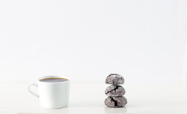 Escena de diseño mínimo: una taza de café y una galleta de chocolate negro sobre fondo blanco liso incluye espacio para copiar