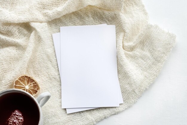 La escena del diseño de papelería en una tecla clara Una tarjeta de felicitación vertical vacía y una taza de té blanca