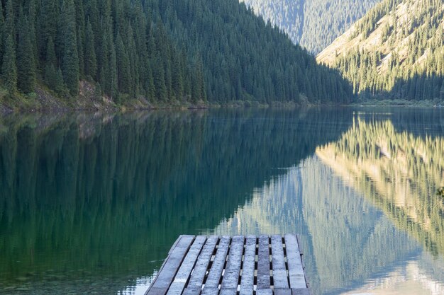 una escena forestal y un muelle de madera en un lago de montaña Lago Kolsai en Kazajstán