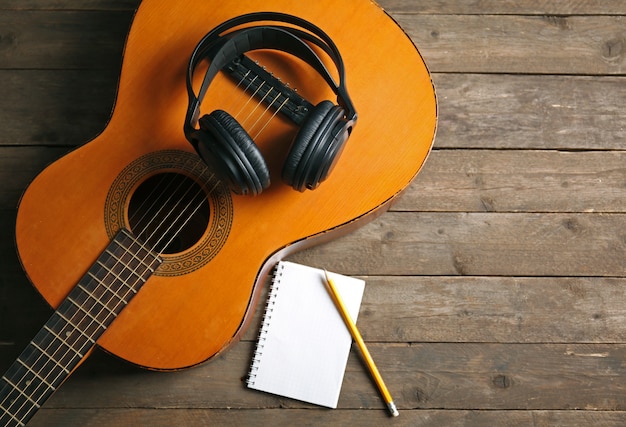 Foto escena de grabación de música con guitarra clásica, bloc de notas y auriculares en madera