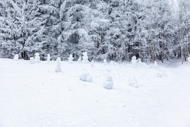 Escena de invierno en una zona de descanso cerca de un bosque. Bancos y muñecos de nieve, camino forestal