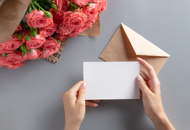 Escena de maqueta de tarjeta de felicitación con mano de mujer sosteniendo una tarjeta de papel en blanco