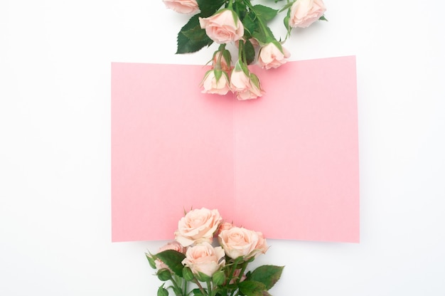 Escena de maquetas de boda o cumpleaños. Hoja de papel abierta en blanco con lugar para texto para tarjeta de felicitación. Ramo de rosas rosadas.