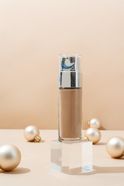Una escena minimalista de botella de base en podio de vidrio con bolas decorativas navideñas sobre fondo beige