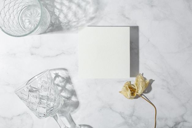 Foto escena de naturaleza muerta con gafas sobre fondo de mármol a la luz del sol y maqueta de invitación de tarjeta de felicitación de negocios en blanco largas sombras duras