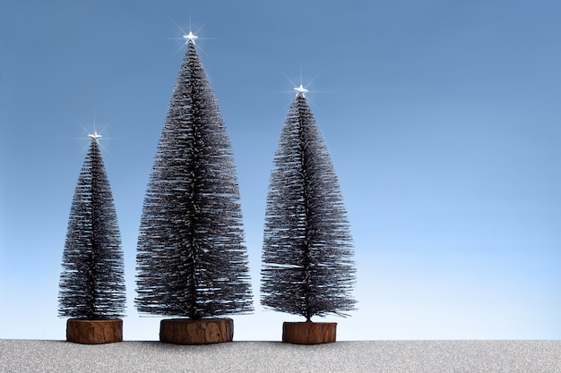 Escena de Navidad con abetos en miniatura y tierra plateada brillante y cielo azul. Copia espacio