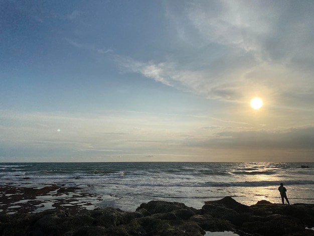 Una escena de playa con una puesta de sol sobre el océano y un cielo nublado.