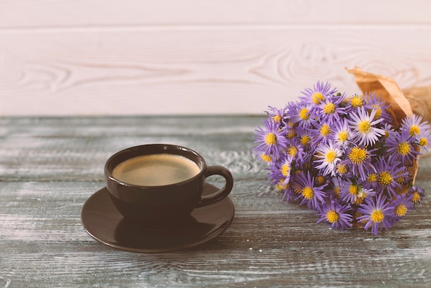 Escena romántica con una taza de café, un ramo de flores de color púrpura en papel artesanal sobre una mesa de madera gris