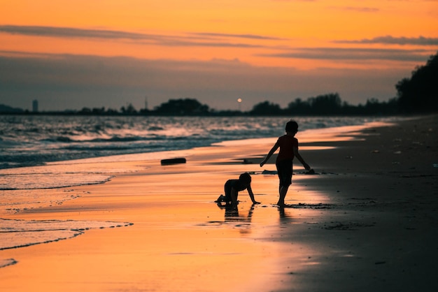 Escena de silueta de dos niños jugando en la playa con puesta de sol dorada