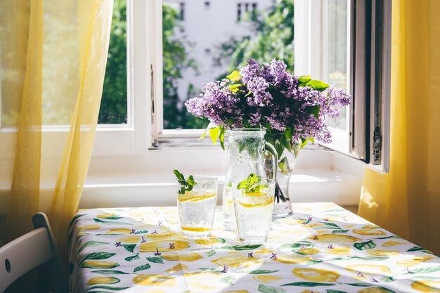 Escena de verano de limonada y flores en un jarrón junto a una ventana