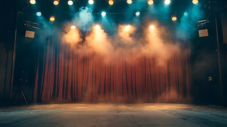 Un escenario oscuro con cortinas rojas, humo y reflectores