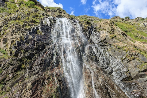 Escenas de la cascada de la visión del primer en las montañas, parque nacional Dombai, Cáucaso, Rusia, Europa. Paisaje de verano, clima soleado, espectacular cielo azul y día soleado