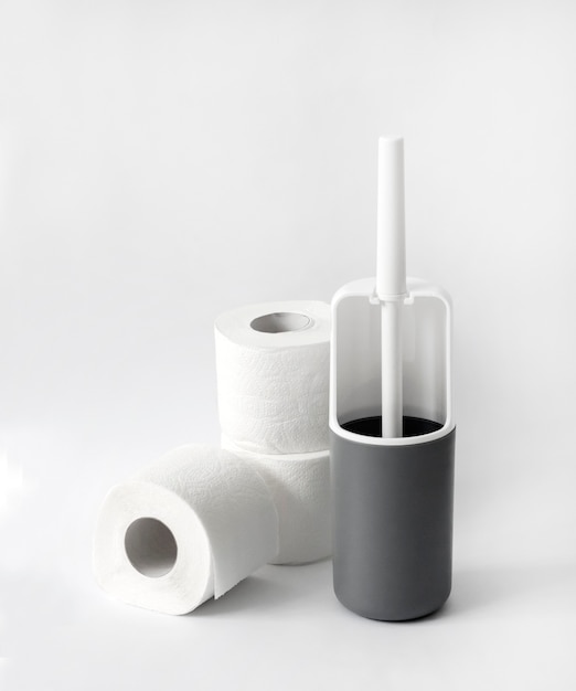 Escobilla de baño de plástico blanco y gris y papel higiénico sobre fondo blanco. Copia espacio