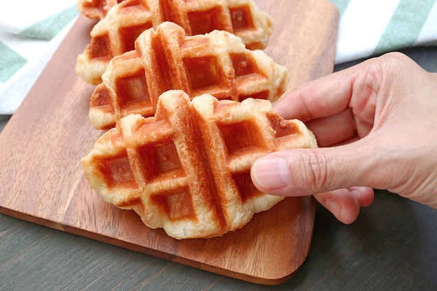 Escogiendo a mano un delicioso croffle recién horneado o un waffle croissant de la placa de pruebas