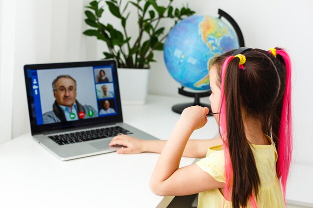 Escola online legal. Criança estudando online em casa usando um laptop. Jovem alegre usando o computador portátil, estudando através do sistema de e-learning online. Aprendizagem à distância ou à distância