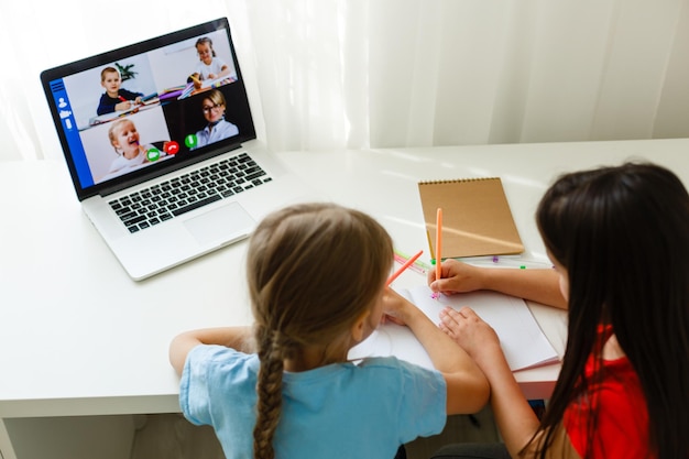 Escola online legal. crianças estudando online em casa usando um laptop. alegres meninas usando o computador laptop, estudando através do sistema de e-learning online. aprendizagem à distância ou à distância