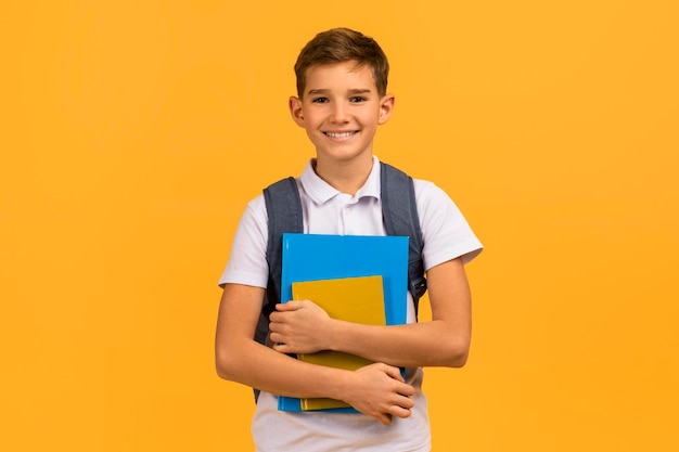 Escolar adolescente sorridente com mochila segurando livros e sorrindo para a câmera