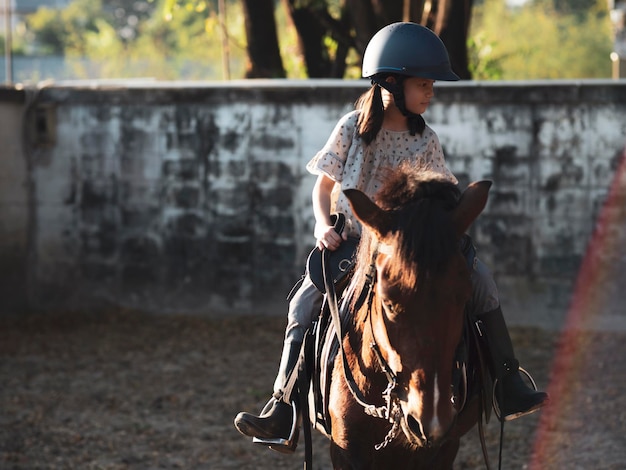 Foto escolar asiática com equitação ou praticando equitação em um rancho de cavalos