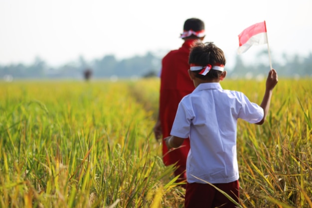 Un escolar asiático con uniforme camina juntos en el campo de arroz mientras levanta una bandera blanca roja