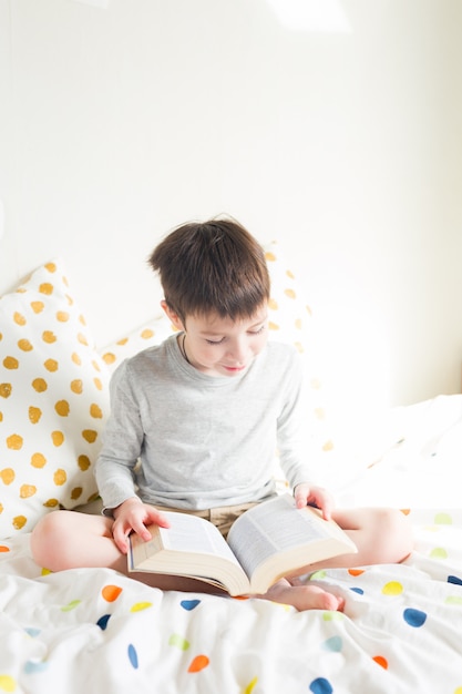 Escolar en cama y hacer el libro de lectura de la tarea escolar en casa. Educación a distancia en línea. Cuarentena. Concepto quedarse en casa durante una emergencia