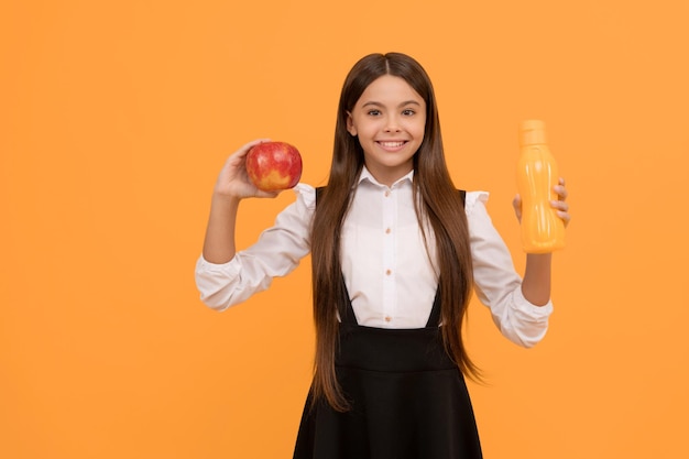 Escolar feliz en uniforme sostenga manzana y botella de agua vitamina