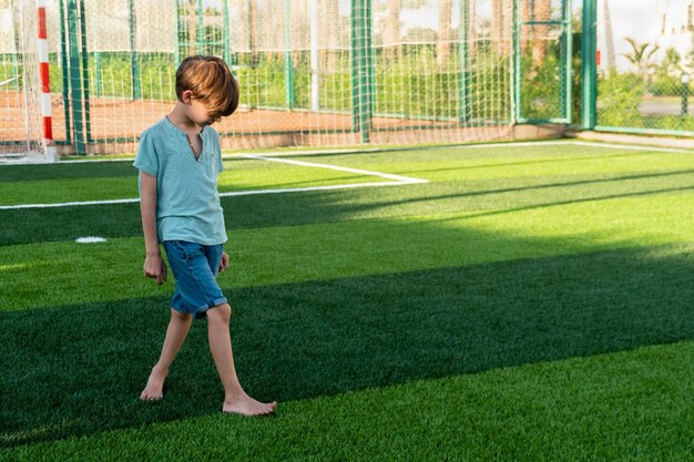 Foto un escolar triste caminando por el campo de deportes verde y mirando hacia abajo