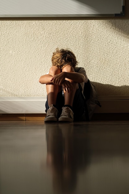 Foto un escolar triste y solitario sentado en el suelo en el aula de la escuela y abrazando las rodillas