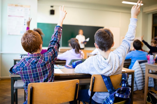 Los escolares en el aula con las manos levantadas respondiendo a la pregunta del maestro.